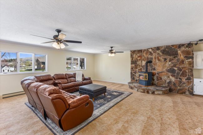 Living room featuring a wood stove, a ceiling fan, a baseboard heating unit, and a textured ceiling | Image 4