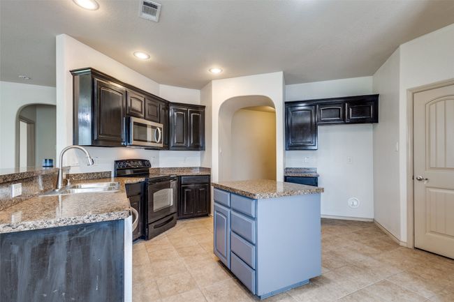 Kitchen with black range with electric stovetop, arched walkways, stainless steel microwave, a kitchen island, and light stone countertops | Image 12