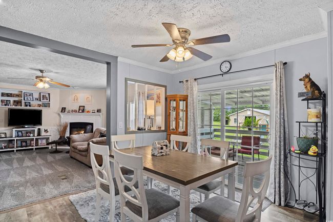 Dining area with a ceiling fan, wood finished floors, a textured ceiling, a warm lit fireplace, and ornamental molding | Image 21