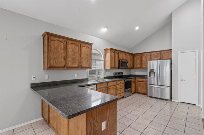 Kitchen with appliances with stainless steel finishes, a peninsula, brown cabinets, dark countertops, and light tile patterned floors | Image 24