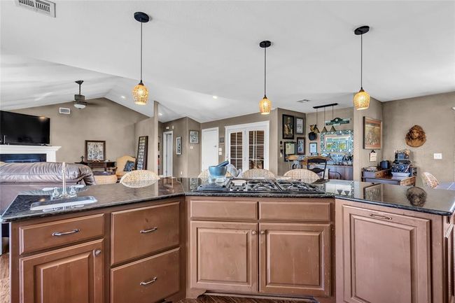 Kitchen with open floor plan, black gas stovetop, a ceiling fan, lofted ceiling, and dark stone countertops | Image 12