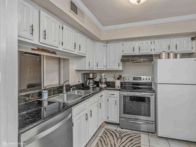 Kitchen featuring a sink, dark countertops, visible vents, under cabinet range hood, and appliances with stainless steel finishes | Image 11