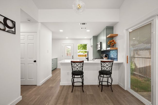 Kitchen with stainless steel microwave, open shelves, light countertops, wood finished floors, and a peninsula | Image 10