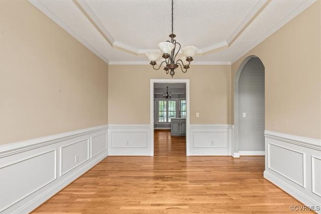 Empty room featuring a chandelier, arched walkways, a tray ceiling, light wood-style flooring, and crown molding | Image 22