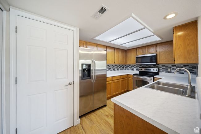 Kitchen with appliances with stainless steel finishes, brown cabinets, light countertops, light wood-type flooring, and backsplash | Image 6