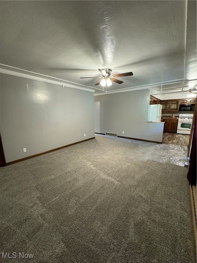 Unfurnished living room with ornamental molding, a textured ceiling, dark carpet, and ceiling fan | Image 2