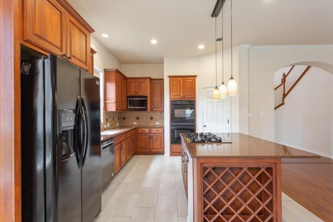 Kitchen with black appliances, brown cabinets, decorative backsplash, dark stone countertops, and arched walkways | Image 16