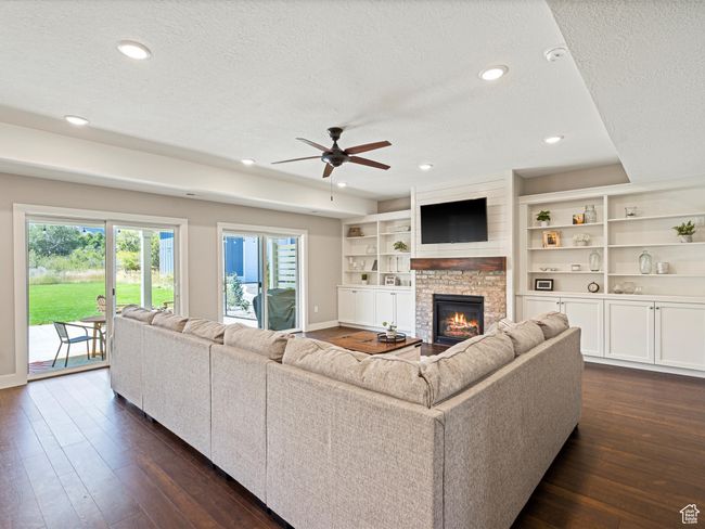 Living area featuring a textured ceiling, dark wood finished floors, baseboards, ceiling fan, and a fireplace | Image 4