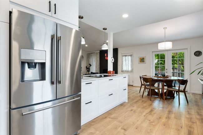 Kitchen with light wood-style floors, white cabinetry, stainless steel refrigerator with ice dispenser, black stovetop, and decorative light fixtures | Image 16