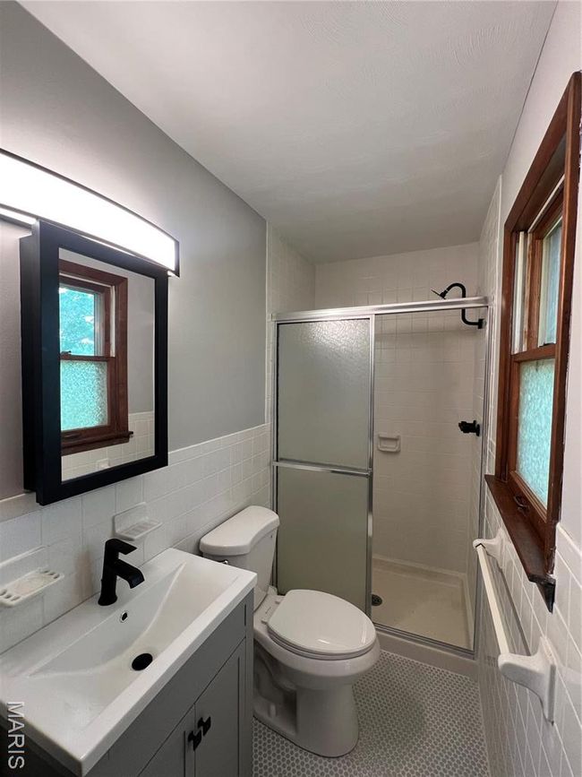 Bathroom featuring a stall shower, tile walls, toilet, tile patterned floors, and vanity | Image 8