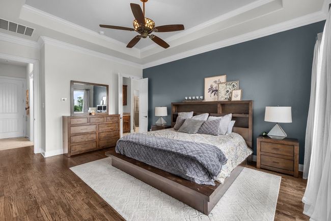 Bedroom featuring a tray ceiling, wood finished floors, ornamental molding, a ceiling fan, and baseboards | Image 13