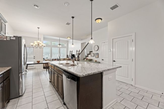 Kitchen with appliances with stainless steel finishes, a sink, dark brown cabinetry, light tile patterned floors, and a chandelier | Image 8