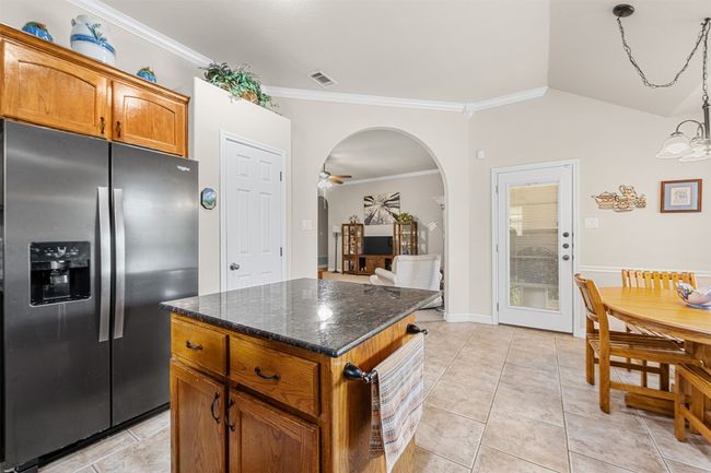 Kitchen featuring stainless steel fridge, a center island, ornamental molding, brown cabinets, and arched walkways | Image 16