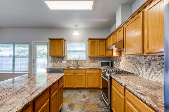 Kitchen with appliances with stainless steel finishes, under cabinet range hood, backsplash, stone finish floors, and light stone countertops | Image 15