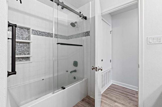 Full bath featuring enclosed tub / shower combo, baseboards, and wood finished floors | Image 23