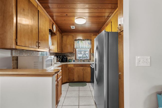 Kitchen with freestanding refrigerator, a sink, backsplash, brown cabinetry, and light tile patterned floors | Image 32