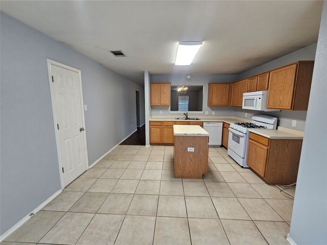 Kitchen featuring white appliances, light countertops, a kitchen island, light tile patterned flooring, and brown cabinets | Image 12