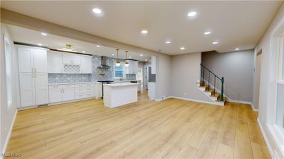 Kitchen featuring a center island, hanging light fixtures, wall chimney exhaust hood, light wood-type flooring, and white cabinetry | Image 2