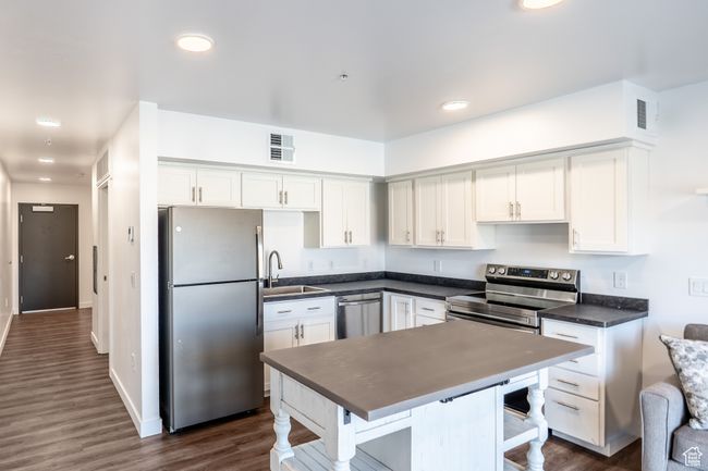 Kitchen featuring dark countertops, visible vents, dark wood finished floors, appliances with stainless steel finishes, and white cabinets | Image 4