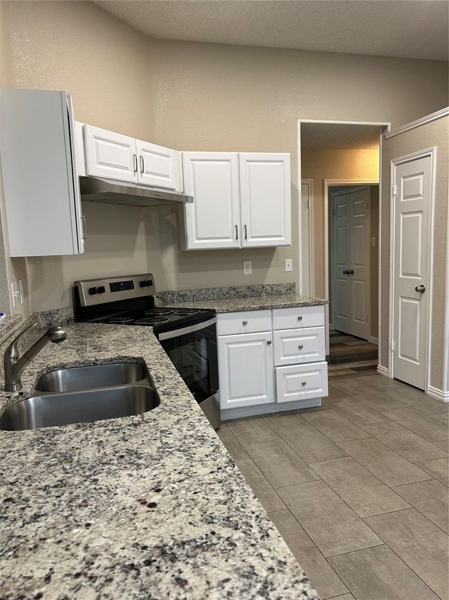 Kitchen with stainless steel electric range oven, white cabinetry, under cabinet range hood, and light stone counters | Image 7