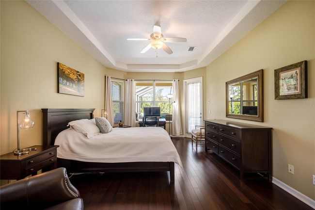 Spacious Primary Room with rich wood flooring, a private door entry to lanai, and large windows revealing the lush green natural park behind the home. | Image 18