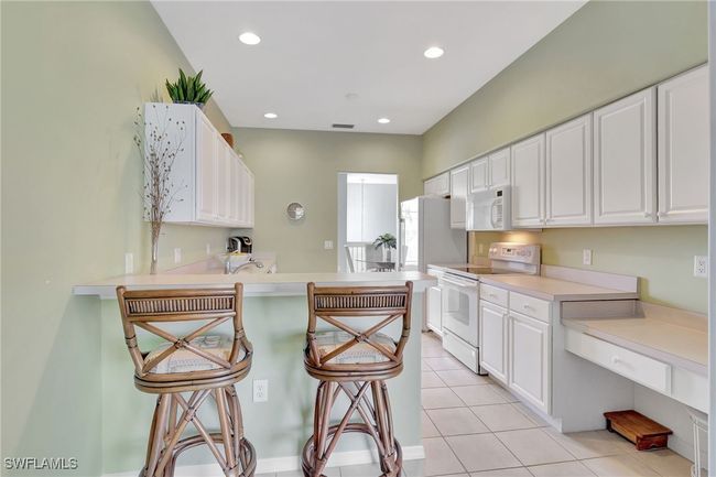 Kitchen featuring white appliances, a kitchen breakfast bar, white cabinetry, a peninsula, and recessed lighting and a desk area | Image 21