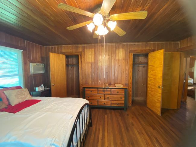 Bedroom with a wall mounted AC, wood walls, wooden ceiling, dark wood finished floors, and a ceiling fan | Image 21