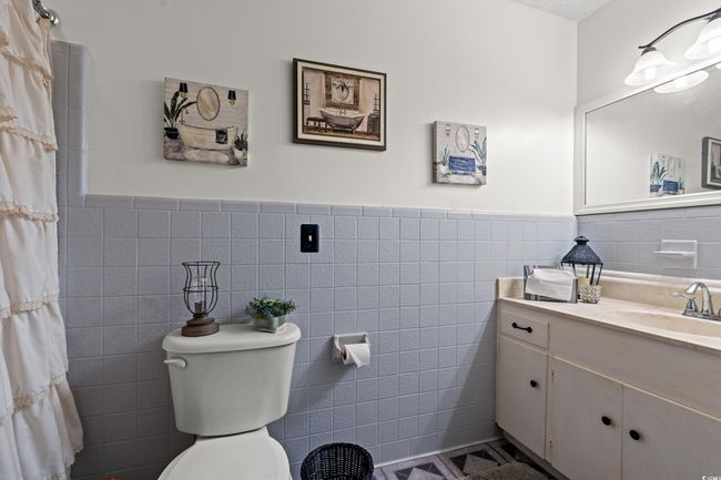 Full bathroom with vanity, tile walls, a shower with curtain, a wainscoted wall, and toilet | Image 22