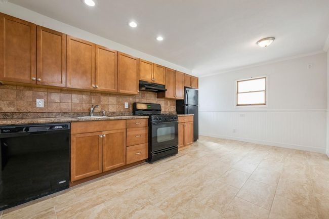 Kitchen with crown molding, black appliances, under cabinet range hood, brown cabinetry, and a sink | Image 12