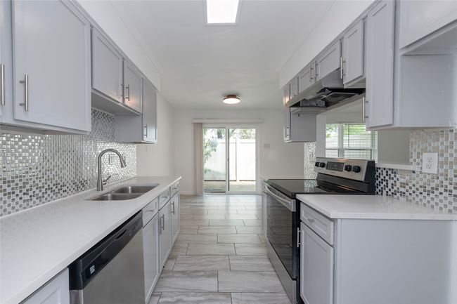 Kitchen with appliances with stainless steel finishes, light countertops, under cabinet range hood, decorative backsplash, and a sink | Image 9