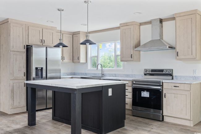 Kitchen featuring wall chimney exhaust hood, appliances with stainless steel finishes, light brown cabinetry, light countertops, and recessed lighting | Image 13