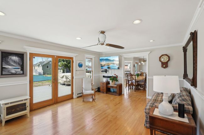 Living room with crown molding, light wood-type flooring, a ceiling fan, a baseboard heating unit, and french doors | Image 10
