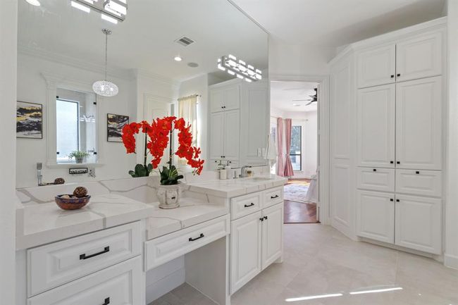 Luxurious primary bathroom with a double vanity, sleek quartz countertops, a seamless mirror, and built-in storage. A cozy sitting area at the vanity adds both function and comfort. | Image 21