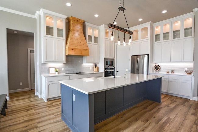 Kitchen featuring an island with sink, custom exhaust hood, appliances and backsplash | Image 4