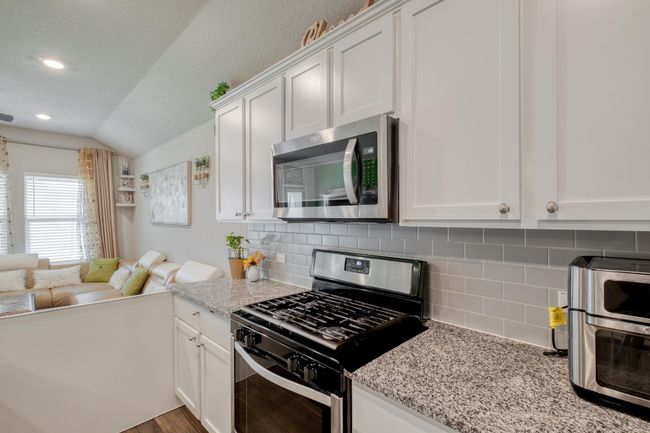 Kitchen featuring appliances with stainless steel finishes, white cabinetry, decorative backsplash, and light stone counters | Image 13