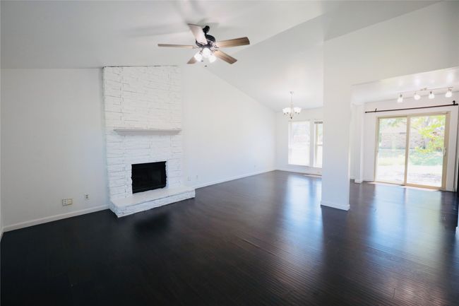 living room with a chandelier, a ceiling fan, a fireplace, dark wood-style floors, and vaulted ceiling | Image 8