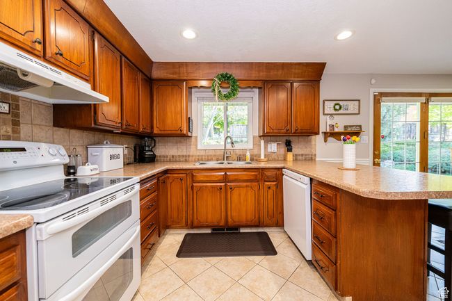 Kitchen with a sink, white appliances, brown cabinetry, a peninsula, and under cabinet range hood | Image 15
