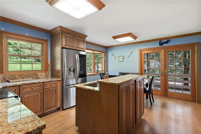 Kitchen with stainless steel fridge with ice dispenser, light wood-type flooring, an island with sink, light stone countertops, and sink | Image 12