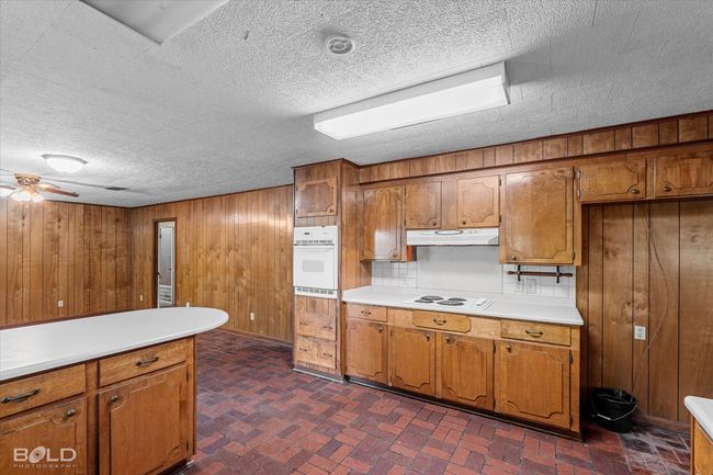 Kitchen featuring white appliances, brown cabinets, wooden walls, under cabinet range hood, and light countertops | Image 15