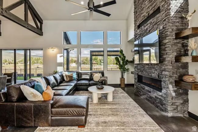 Living area featuring ceiling fan, a stone fireplace, a towering ceiling, and baseboards | Image 13