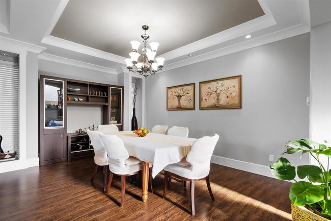 Dining space featuring a raised ceiling, a chandelier, dark wood finished floors, ornamental molding, and baseboards | Image 7