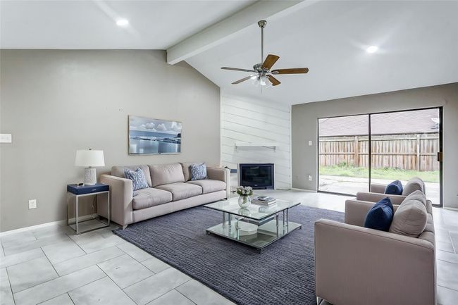 The living area highlights its open-concept design, perfect for entertaining or relaxing with family. Recessed lighting illuminates the space, enhancing the soft neutral tones. The focal-point fireplace invites cozy evenings, while the sliding glass doors bring in sunlight, making the room feel even larger. The flow from indoor to outdoor spaces makes this the ultimate spot for gatherings or quiet nights in. | Image 5