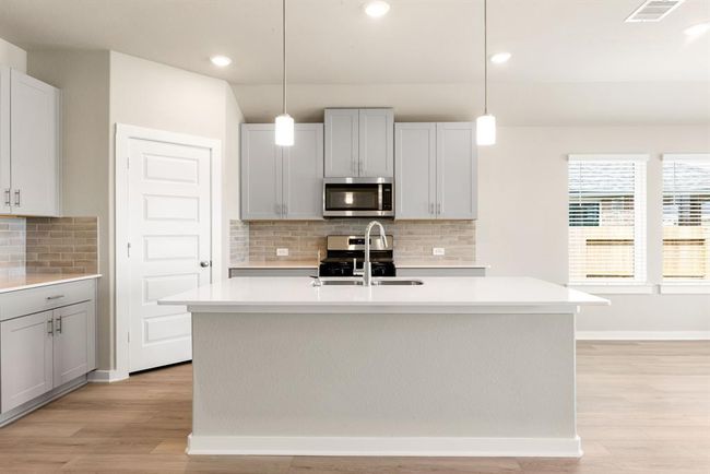 This stunning kitchen features high ceilings, large windows, pebble cabinets, Quartz countertops, and sleek SS appliances. A modern tile backsplash, recessed and pendant lighting, and an oversized Quartz island with a double sink and breakfast bar add style and function. With extended counter space and a walk-in pantry, all overlooking the spacious family room, this kitchen is the heart of the home! | Image 7