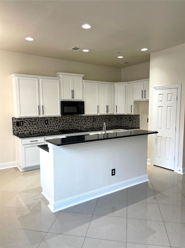 Kitchen with black microwave, dark countertops, white cabinets, decorative backsplash, and recessed lighting | Image 9