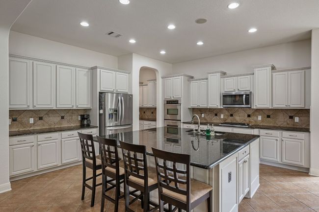 Kitchen featuring decorative backsplash, a sink, visible vents, stainless steel appliances, and arched walkways | Image 10