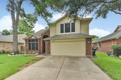 This is a two-story suburban home featuring a brick and siding exterior, with a two-car garage and a neatly landscaped front yard. There's a mature tree offering shade to the property. | Image 2