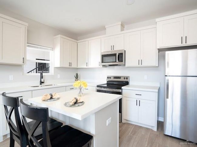 Kitchen with sink, appliances with stainless steel finishes, white cabinetry, a center island, and light hardwood / wood-style floors | Image 7