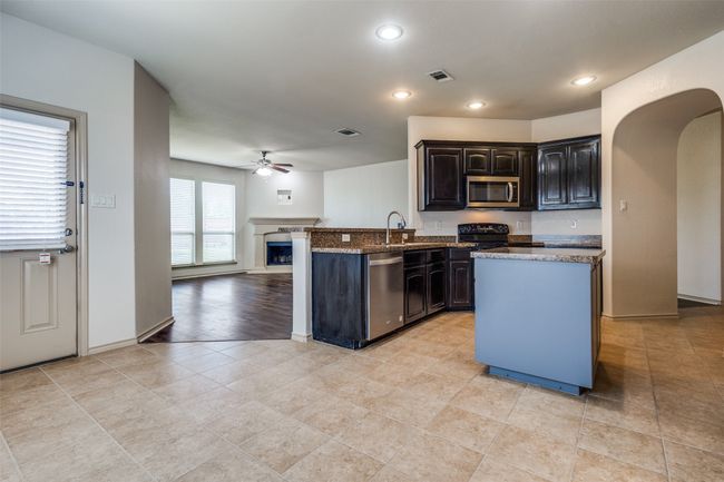 Kitchen featuring stainless steel appliances, ceiling fan, open floor plan, arched walkways, and a fireplace with raised hearth | Image 13