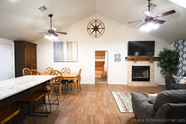Living area featuring a ceiling fan, wood finished floors, a tiled fireplace, baseboards, and high vaulted ceiling | Image 8