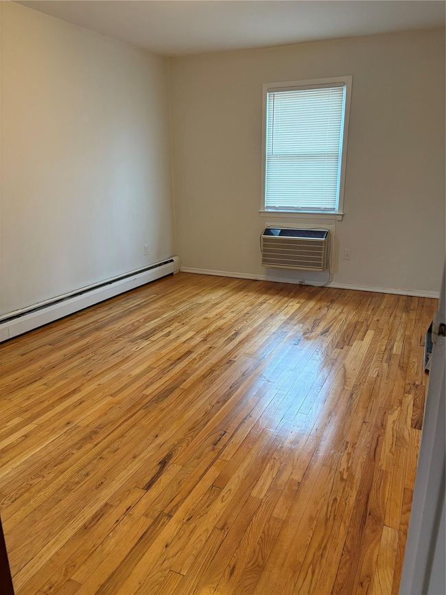 Unfurnished room with an AC wall unit, baseboards, a baseboard heating unit, and light wood-type flooring | Image 10